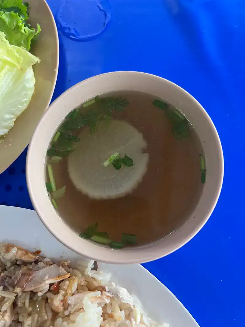 A bowl of clear soup with a slice of white radish and spring onion, on a blue table