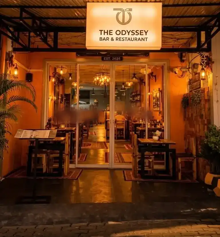 The front at night under the lit sign, with tables set outside the glass doors