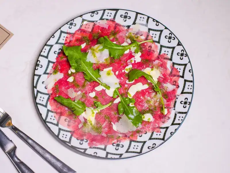 Thin slices of raw beef with rocket and shaved cheese on a black and white patterned plate