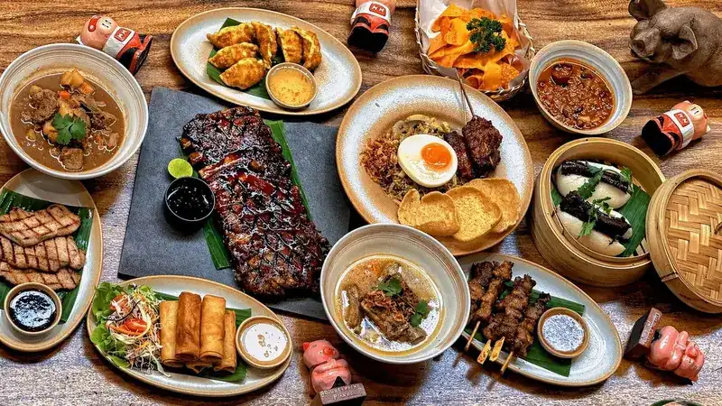 A wooden table covered with ribs, satay, spring rolls, dumplings, soups and fried rice