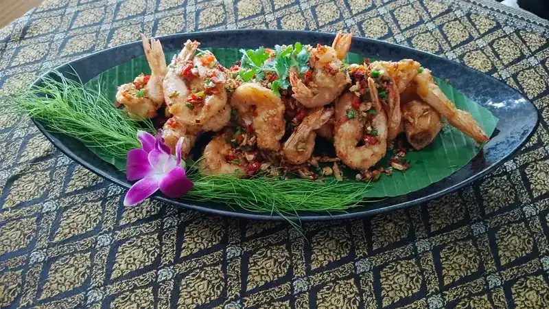 Prawns topped with fried garlic and chilli on a banana leaf, with an orchid