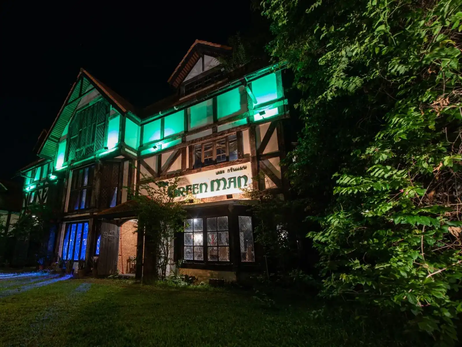 The Green Man's Tudor front at night, lit green among the trees