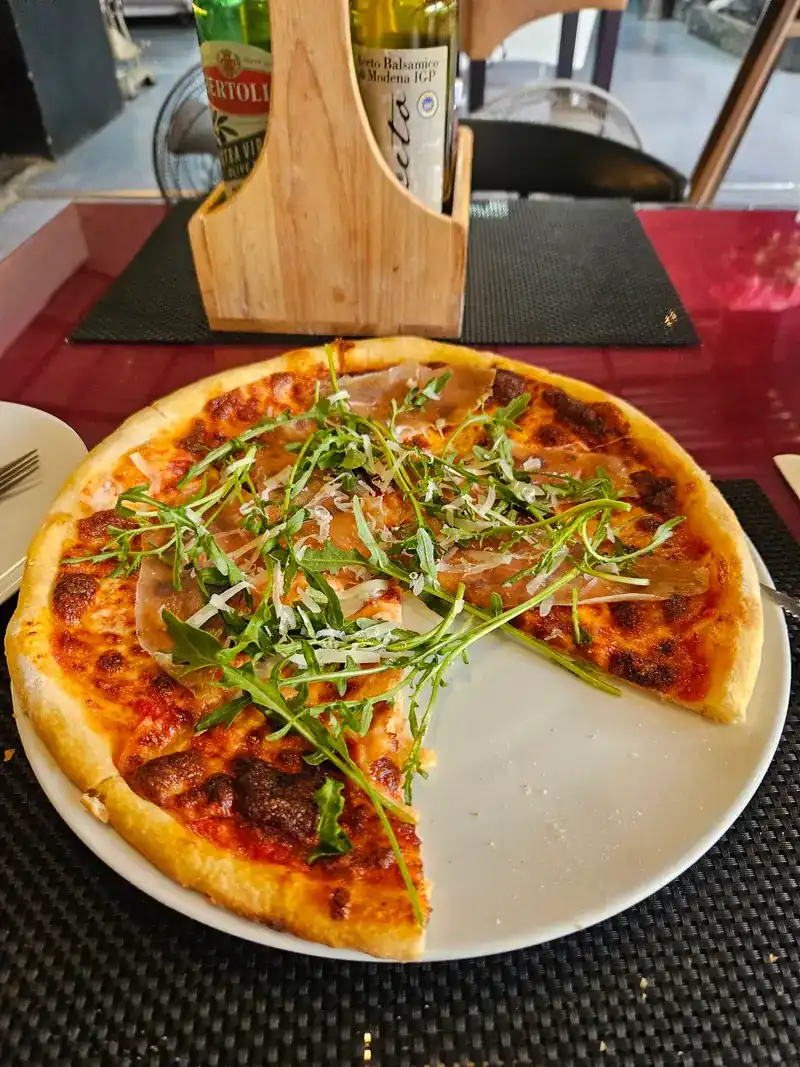 Thin pizza topped with rocket and cured ham, one slice already taken, on a black placemat
