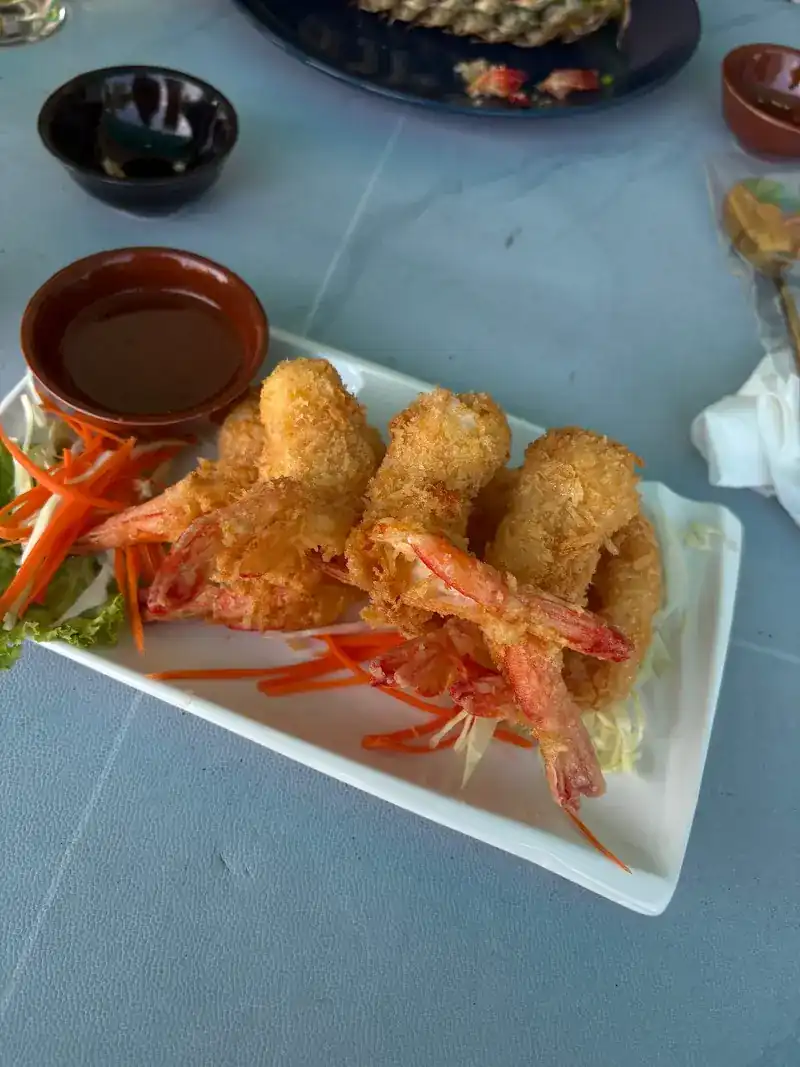 Crisp fried prawns on a white plate with a dipping sauce and shredded carrot