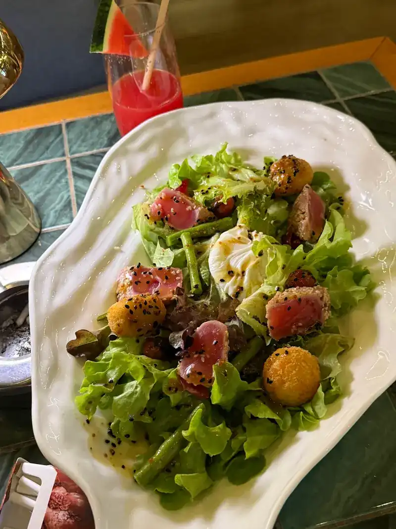 Green salad with seared tuna, a soft egg and crispy potato balls on a white plate