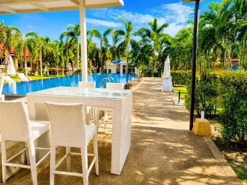 A white bar table and stools beside the pool, under palm trees