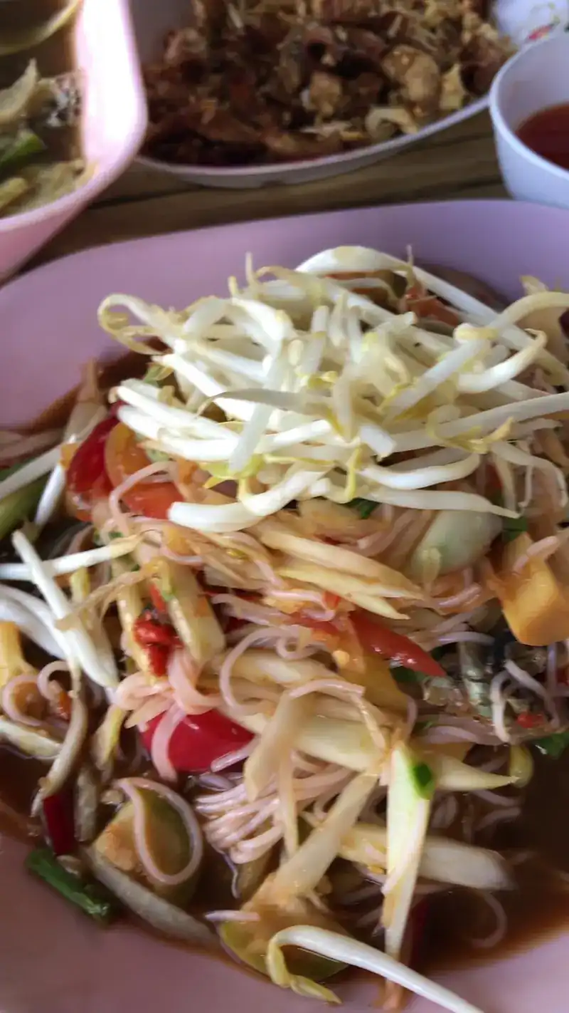 Papaya salad with rice noodles, bean sprouts and tomato on a pink plate