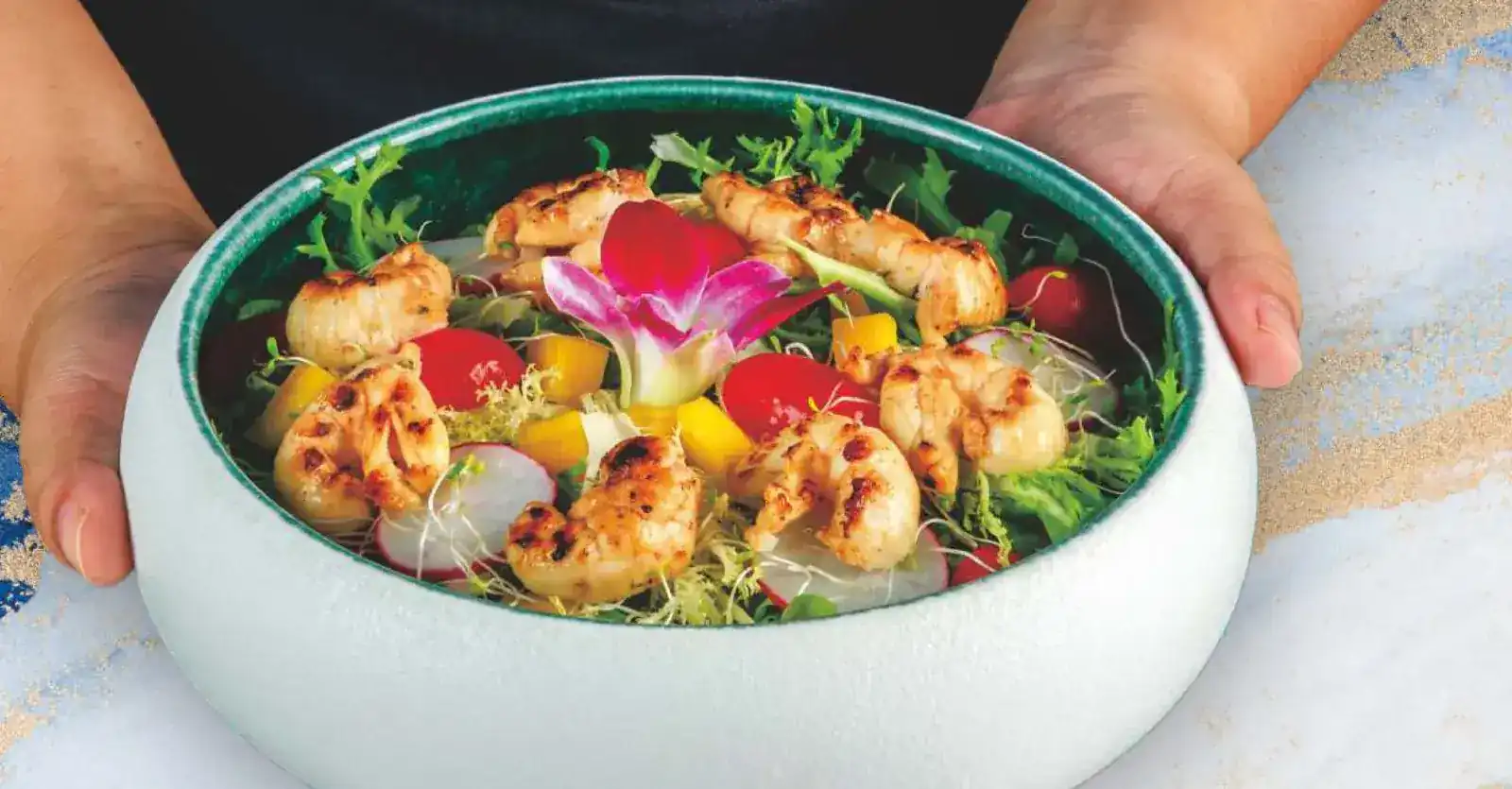 Hands holding a bowl of salad with grilled slipper lobster