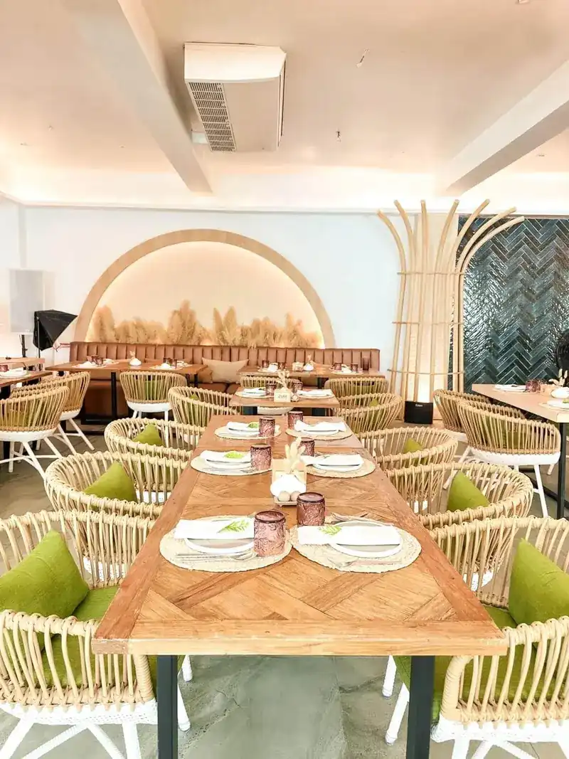 Long wooden table indoors in front of a lit arch filled with pampas grass