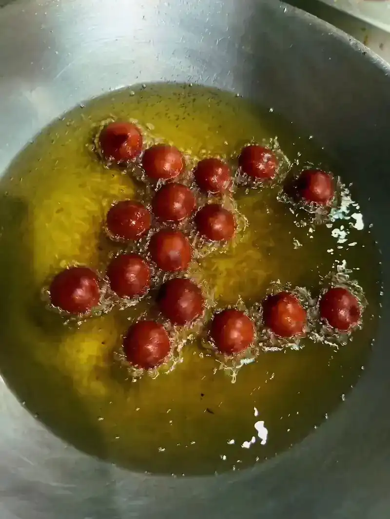 Small dough balls frying in a wide pan of oil in the kitchen