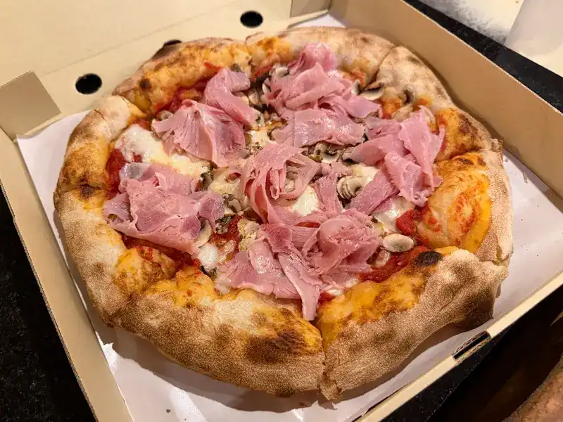 A pizza with ham and mushrooms in an open takeaway box