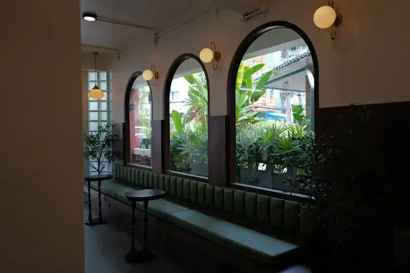 A long green bench under the windows, with small round tables and plants outside