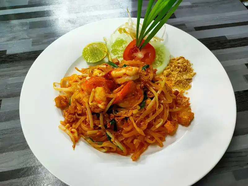 Pad thai with prawns, lime and crushed peanuts on a white plate
