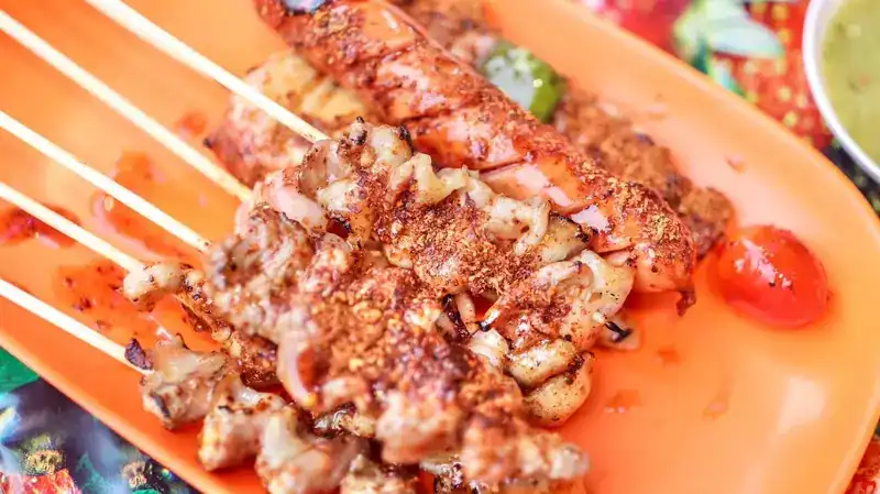 Grilled skewers dusted with red chilli on an orange plate