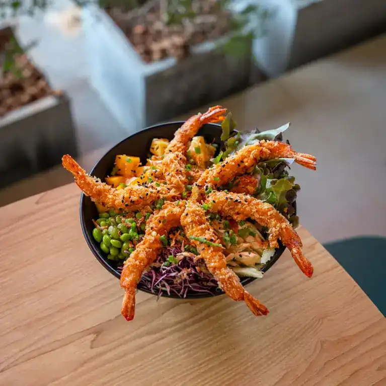 Bowl topped with crispy breaded prawns, edamame, mango and red cabbage