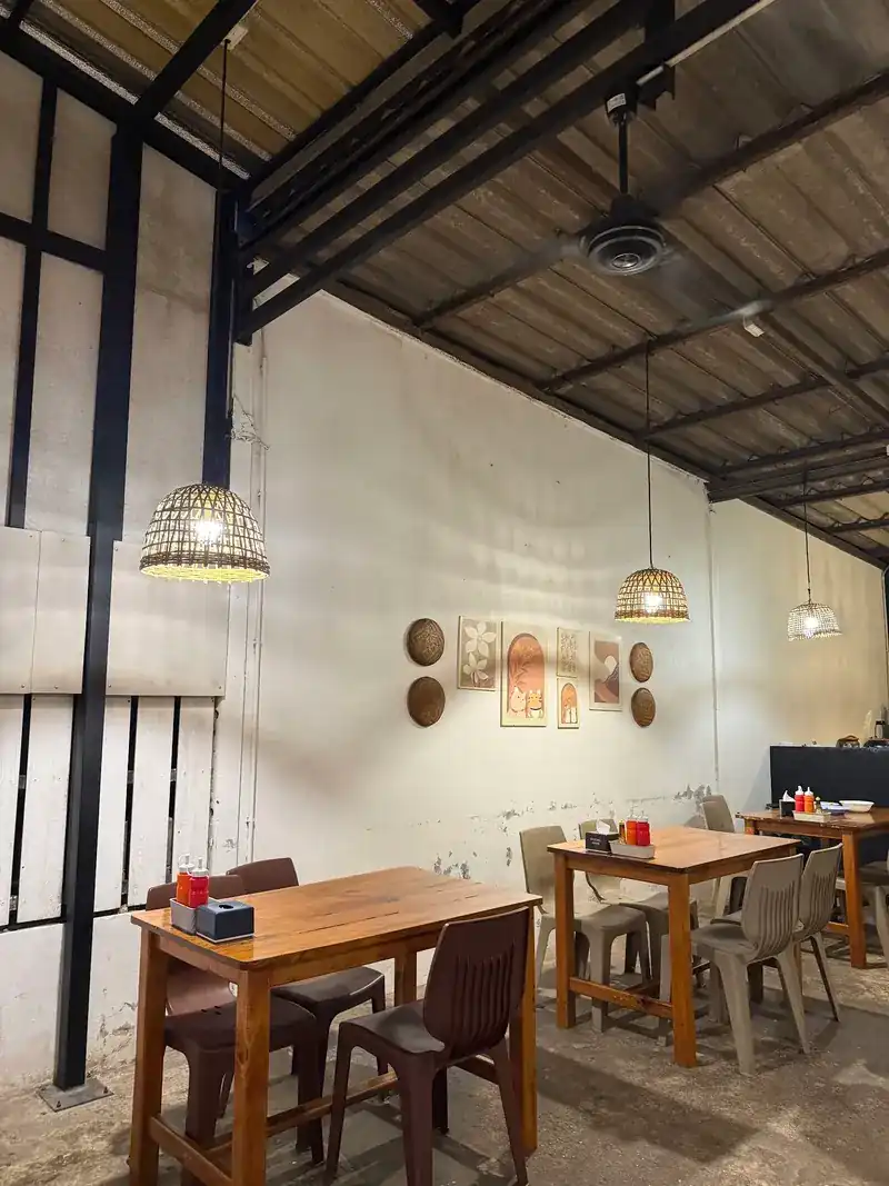Wooden tables under rattan lamps along a whitewashed wall with small pictures / โต๊ะไม้ใต้โคมไฟหวาย ริมผนังสีขาวที่แขวนภาพเล็ก ๆ