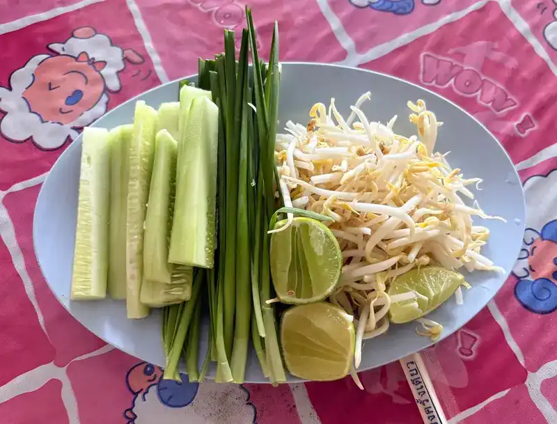 Side plate of cucumber, Chinese chives, bean sprouts and lime on a pink tablecloth