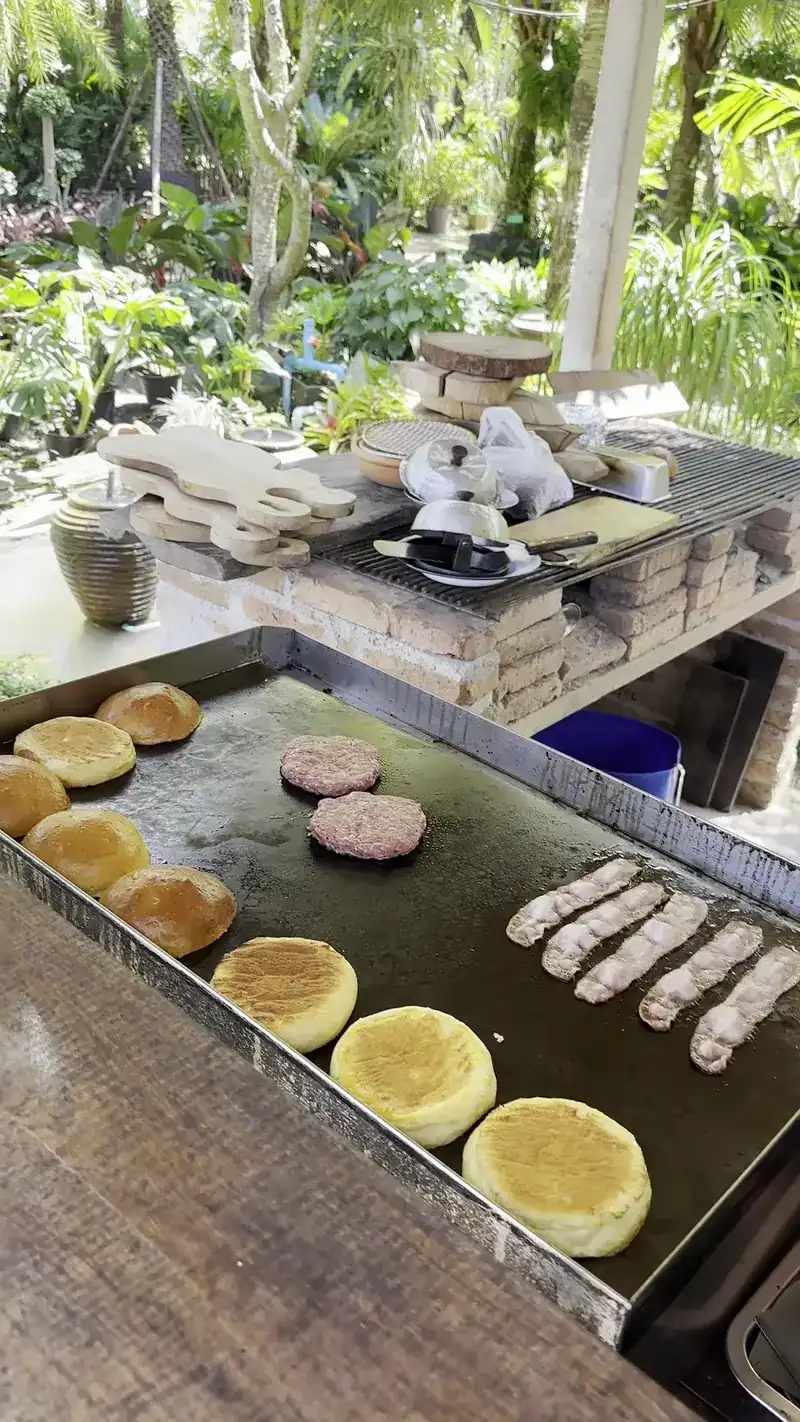 Buns, patties and sausages on the flat-top griddle, the garden behind