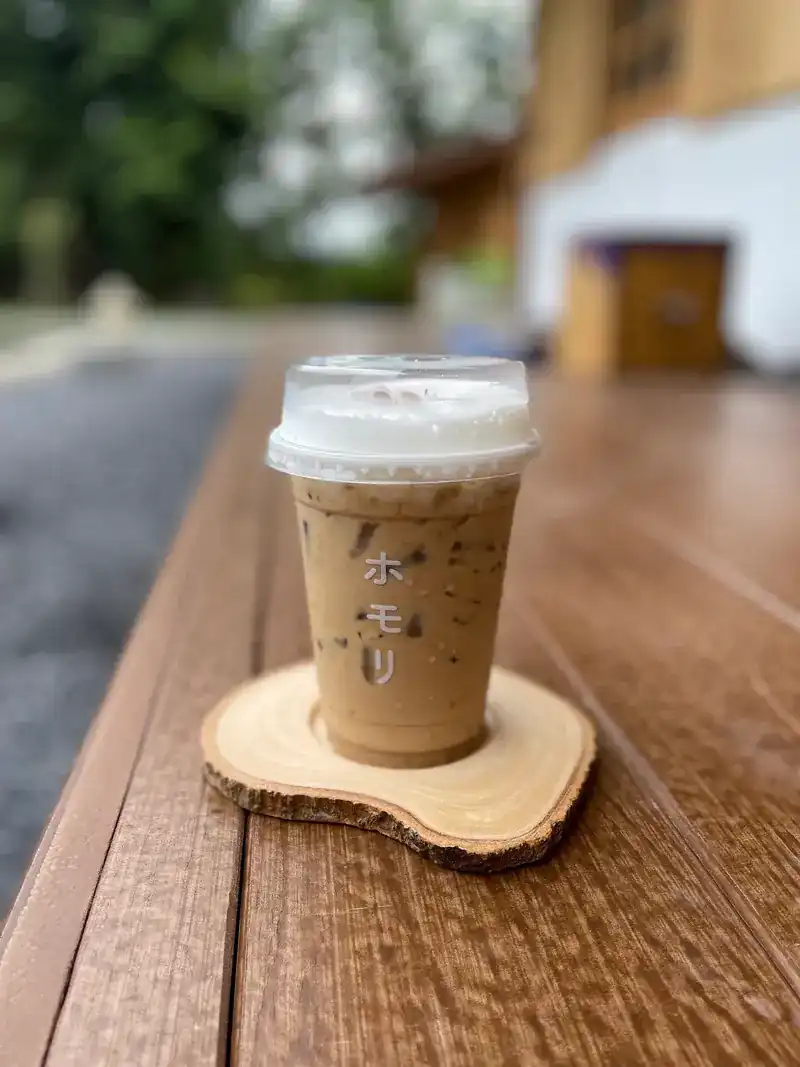 An iced coffee in a cup printed ホモリ on a slice-of-wood coaster on the veranda rail