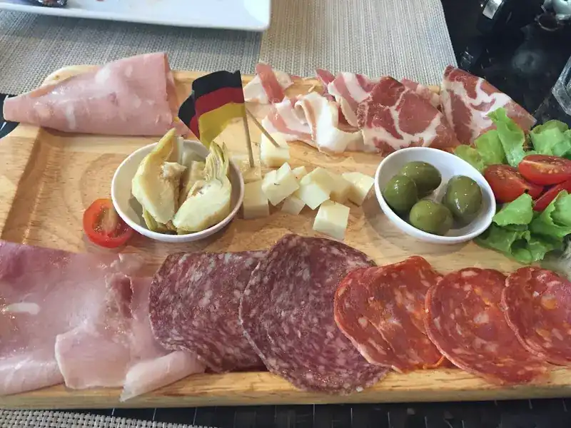 Wooden board of ham, salami, cheese cubes, olives, artichokes and cherry tomatoes
