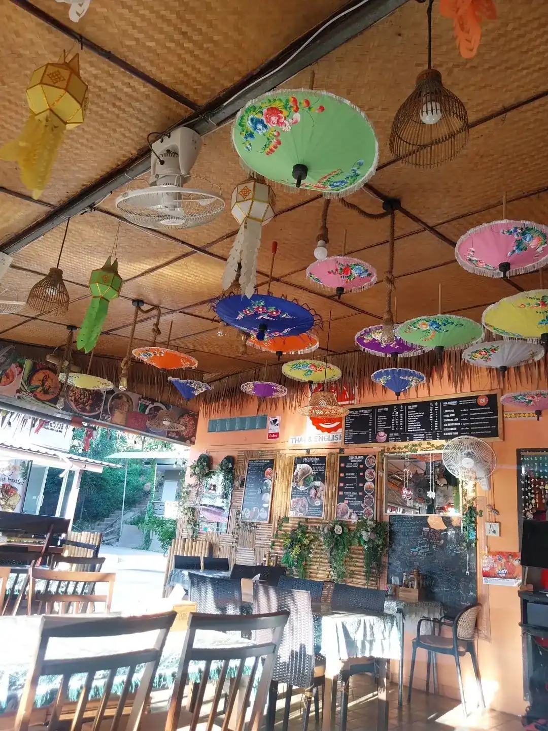 Painted paper parasols and paper lanterns hanging from the woven ceiling over the tables at Nui's Kitchen