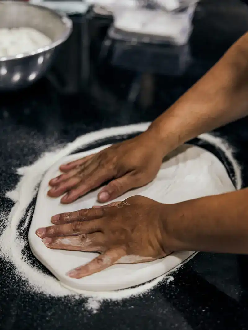 Hands pressing pizza dough on a floured counter