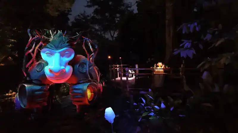 A glowing monkey sculpture in the dark forest beside a candlelit table on the hilltop
