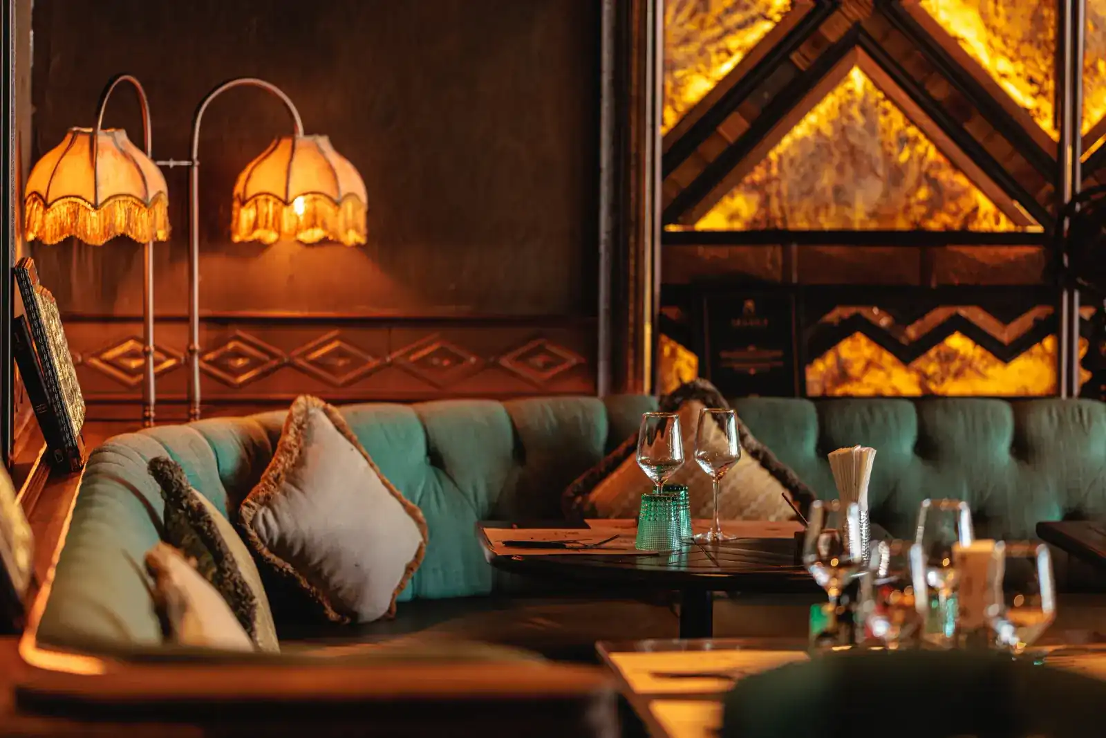 Teal velvet banquette under fringed lamps, glasses set on the table
