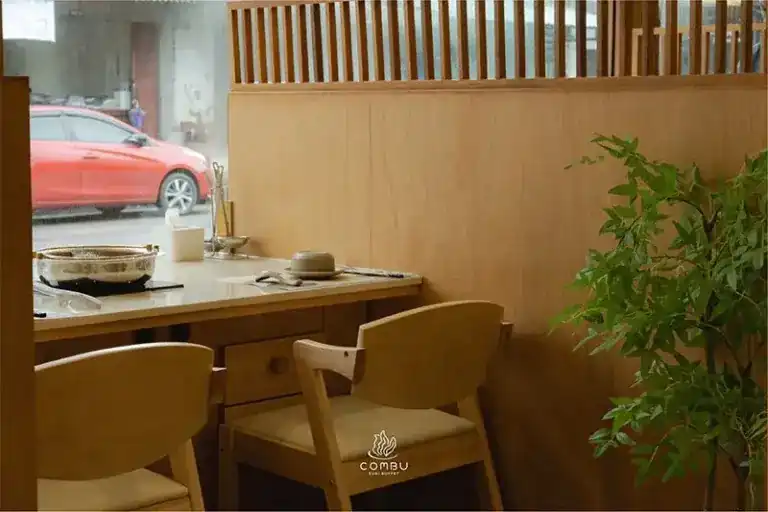 A window table with a suki pot, pale timber chairs and a view of the street