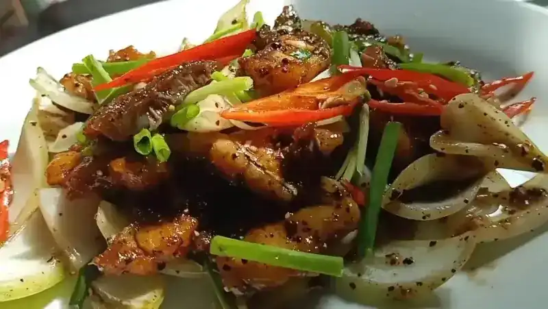 A stir-fry with black pepper, white onion, red chilli and spring onion on a white plate