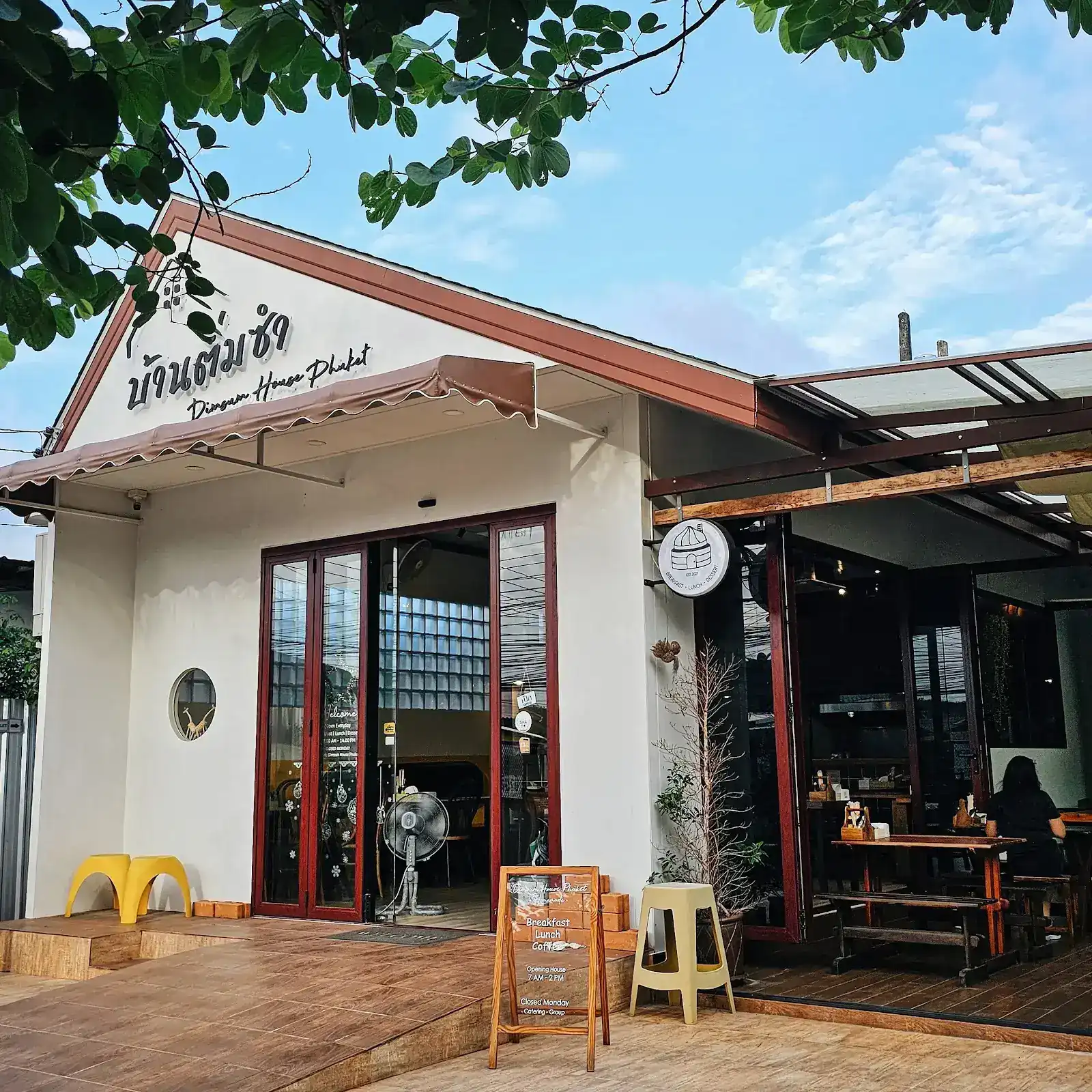 The white gabled house of Dimsum House Phuket, with red-framed glass doors and an open terrace under a tree
