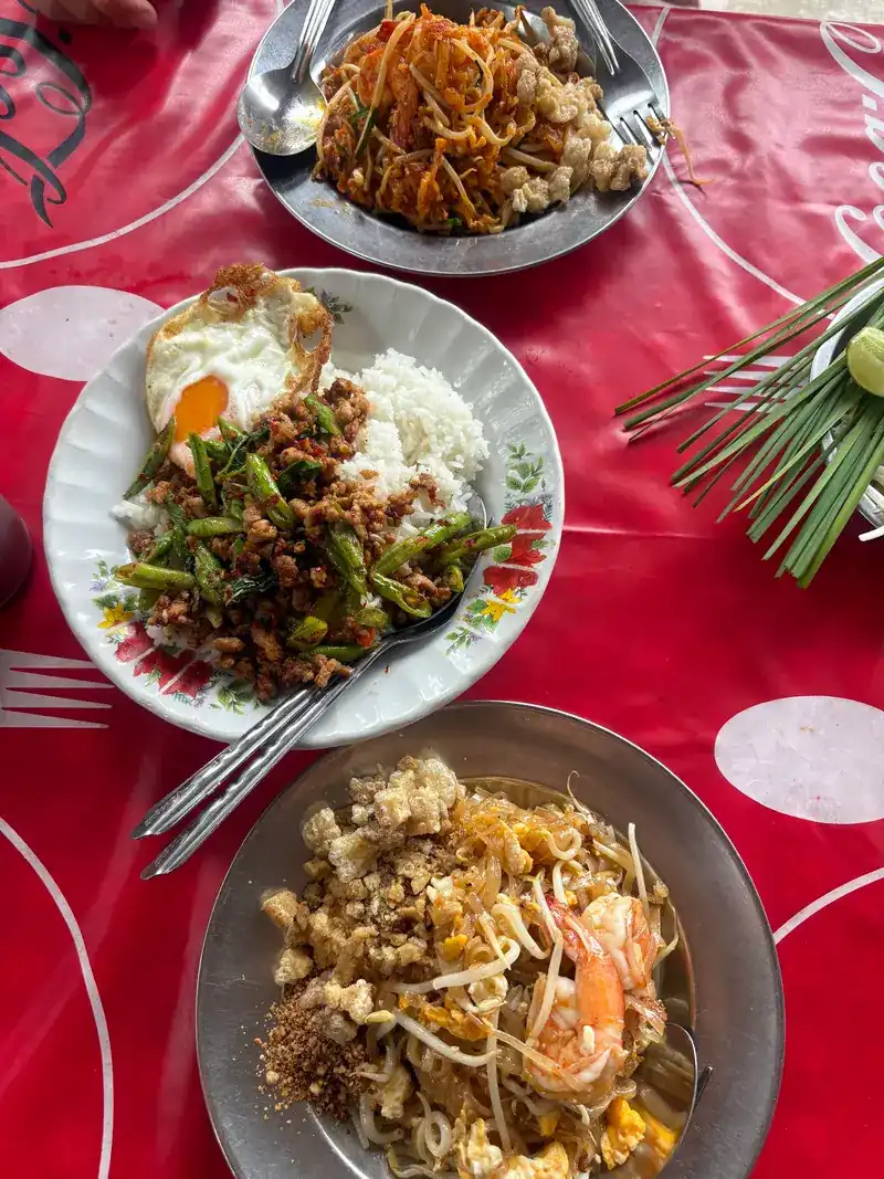 Three plates from above: pad thai, minced pork with long beans over rice with a fried egg, and pad thai with shrimp