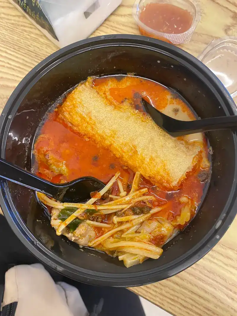 A bowl of red broth with enoki mushrooms and cabbage