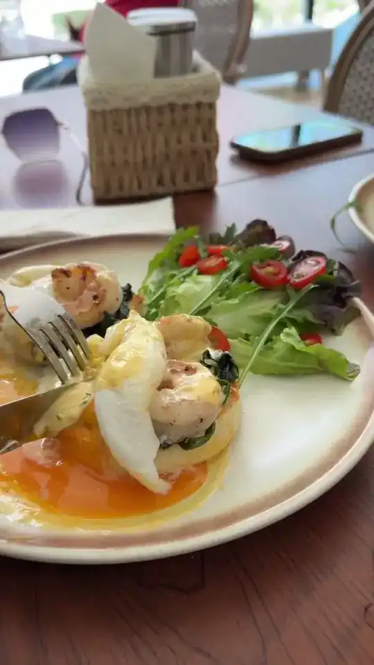 Eggs Benedict topped with prawns, cut open, with a green salad on the side