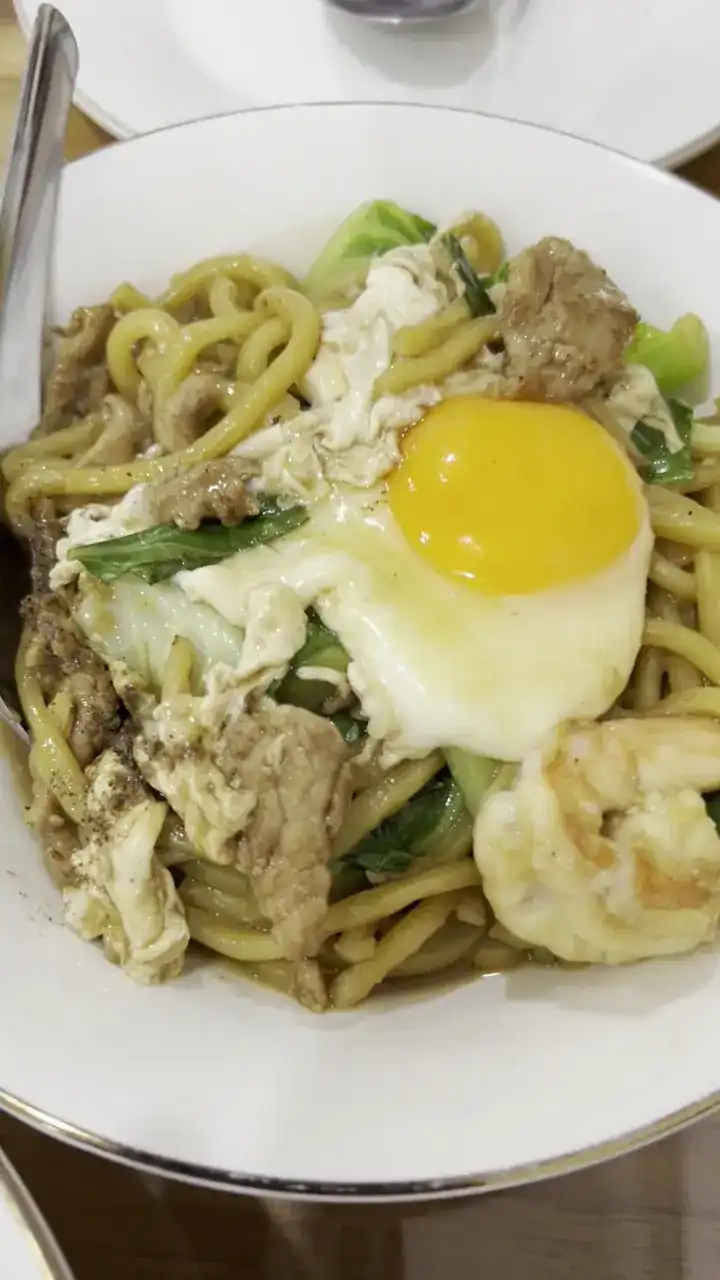 Yellow noodles with a fried egg, greens and prawn