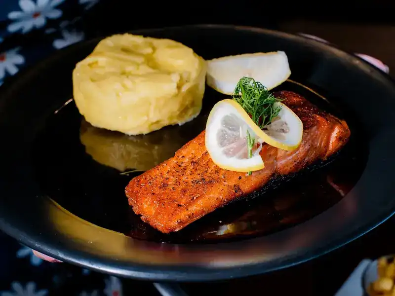 Grilled salmon with lemon and mashed potato on a black plate