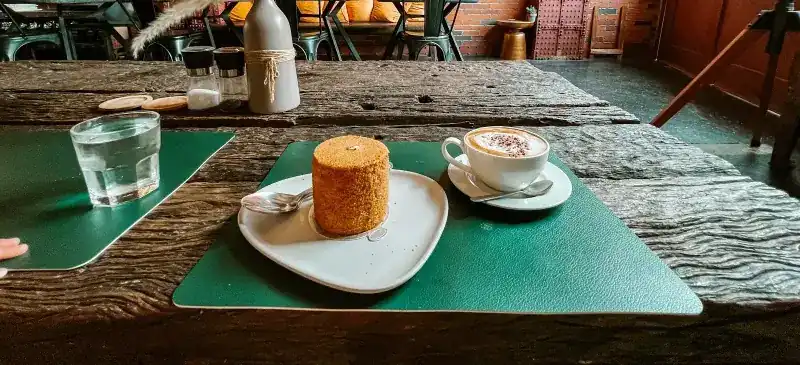 A cake and a cappuccino on a green placemat at a long wooden table