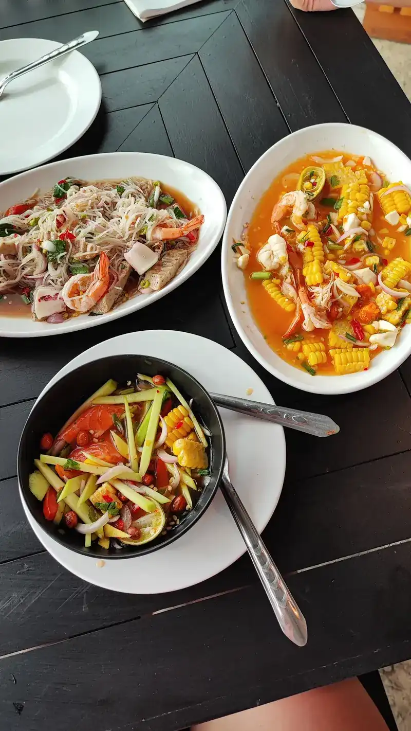 Three spicy salads on a dark table: glass noodles with prawns, sweetcorn, and vegetables with tomato