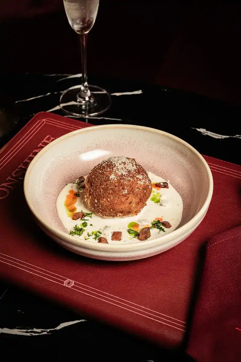 A golden fried rice ball on a white cream sauce