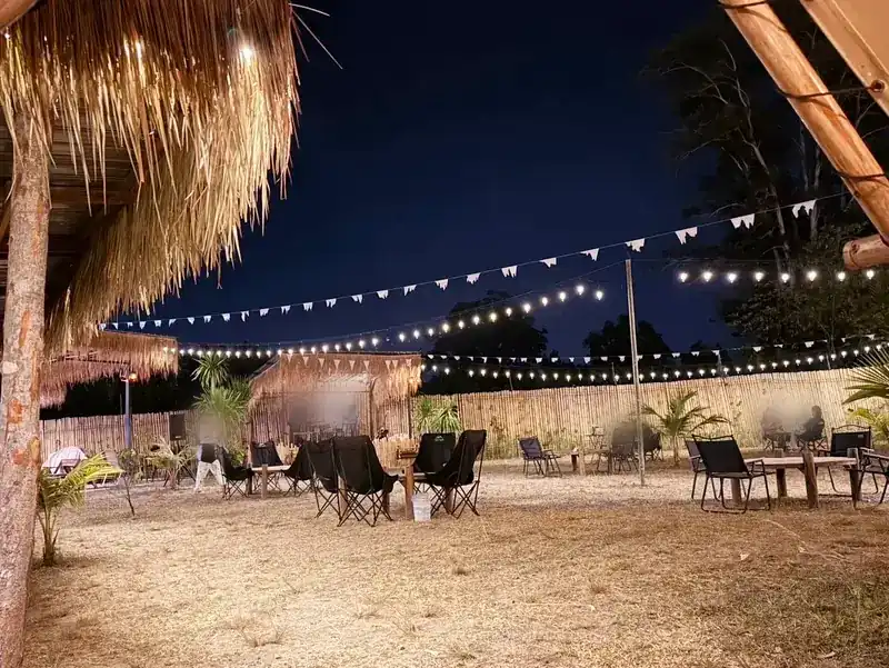 The yard at night: thatched roofs, bunting, lights and camping chairs, with the stage at the back