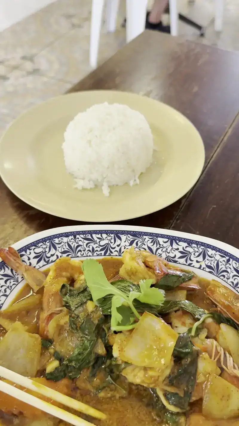 A curry with prawns in a blue and white bowl, with a plate of steamed rice