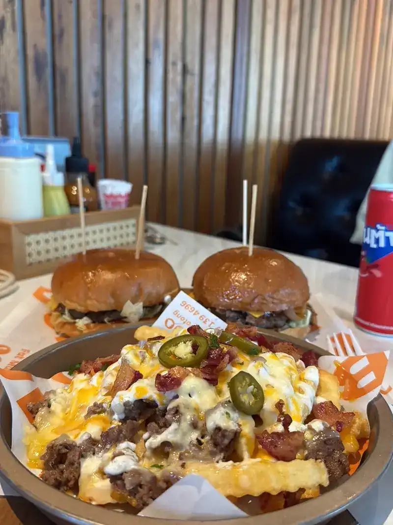 Two burgers behind a bowl of loaded fries with jalapeño slices / เบอร์เกอร์สองชิ้นหลังชามเฟรนช์ฟรายส์จัดเต็ม โรยพริกฮาลาปิโน