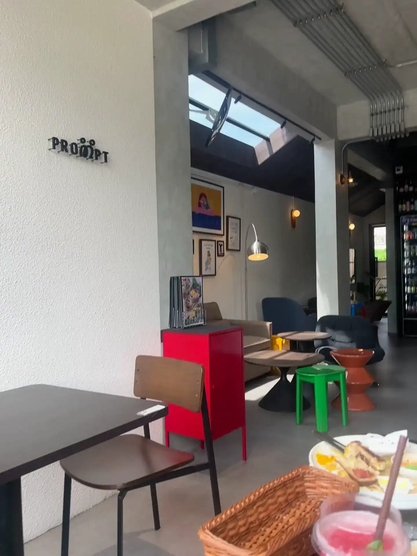 Inside PROMPT: a white wall with the PROMPT sign, a red cabinet, a green stool and framed prints under a skylight
