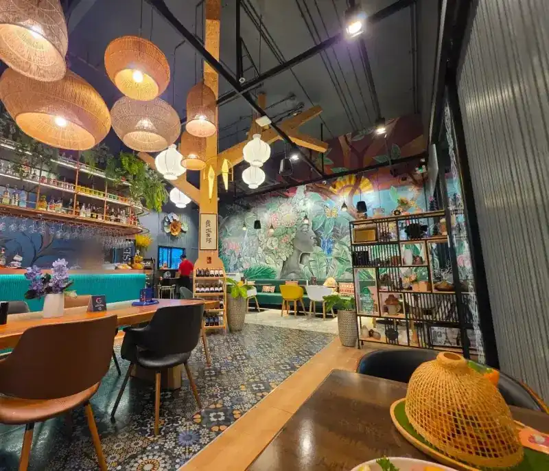 The dining room: rattan lamps, a long wooden table, patterned tiles and a painted jungle wall