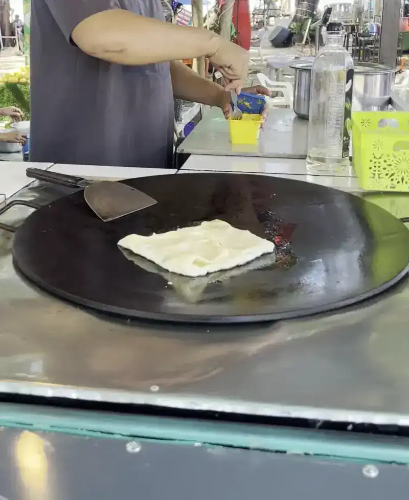 Roti dough being folded on a round flat griddle
