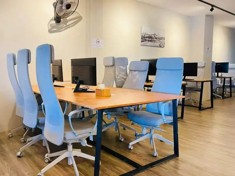The coworking room: long wooden desks, monitors and light blue office chairs