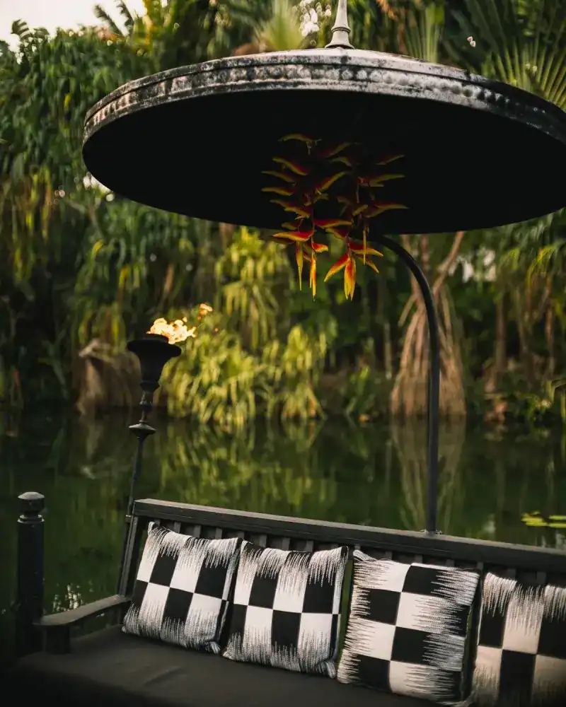 A cushioned bench under a black parasol hung with heliconia, by the lagoon