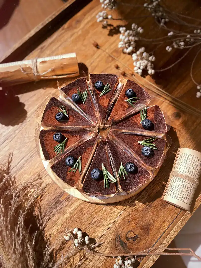A cocoa-dusted cake cut into slices, topped with blueberries and rosemary