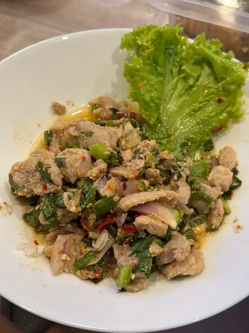 A spicy salad of sliced meat with chilli, mint and spring onion, beside a lettuce leaf