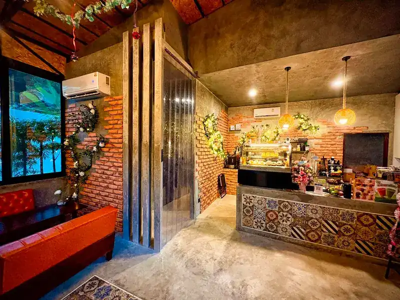 The counter, faced with patterned tiles, with a cake case behind it and brick walls. เคาน์เตอร์กรุกระเบื้องลาย มีตู้เค้กอยู่ด้านหลังและผนังอิฐ